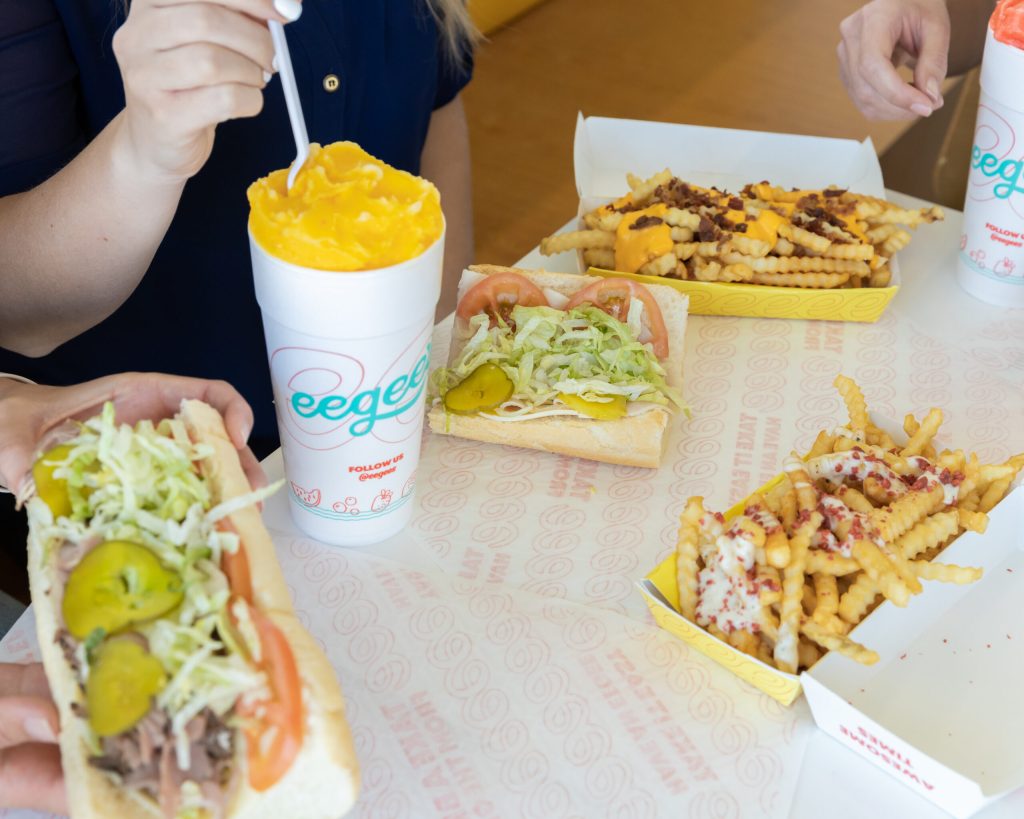table full of eegee's food. Subs, ranch fries and an eegee drink.